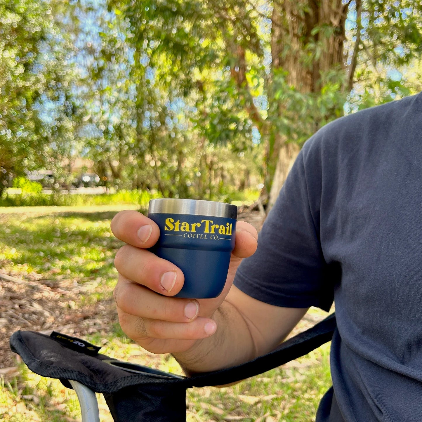 Person holding a blue mug with 'Star Trail Coffee Co.' branding outdoors.