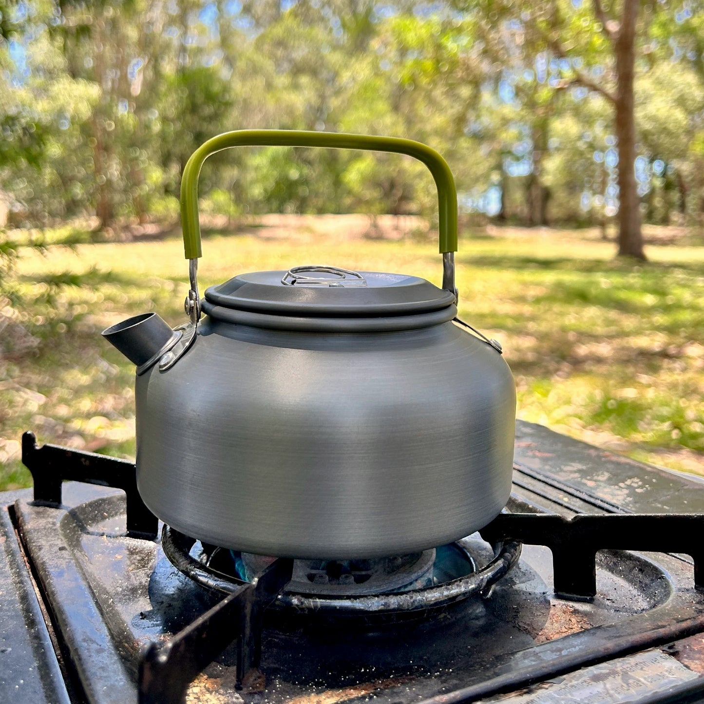 Black kettle with a green handle on a camping stove outdoors